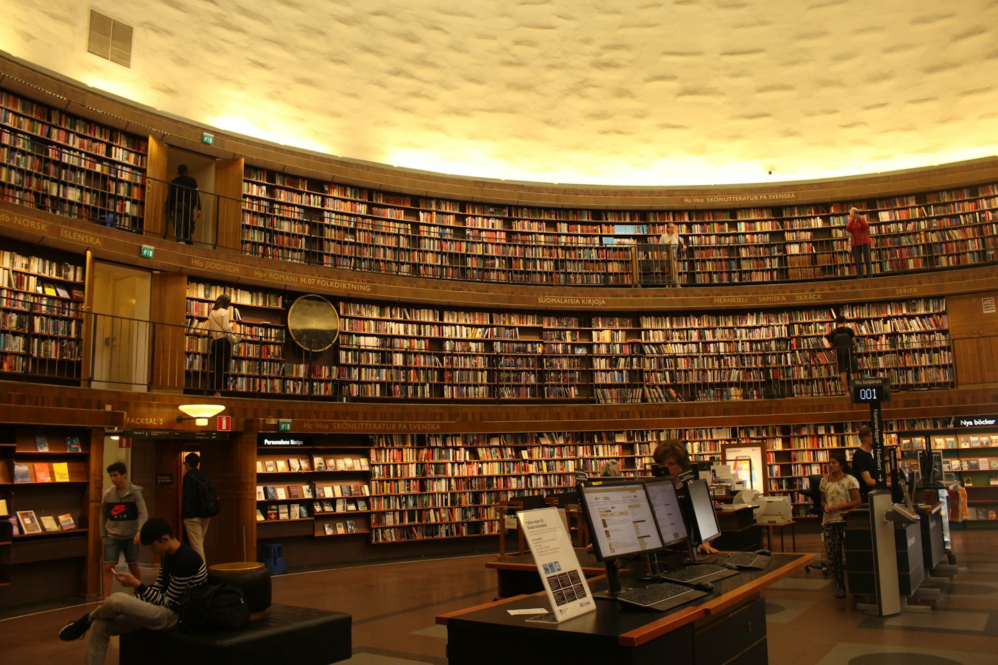 Ludzie przeglądają książki i korzystają z komputerów w okrągłej bibliotece.