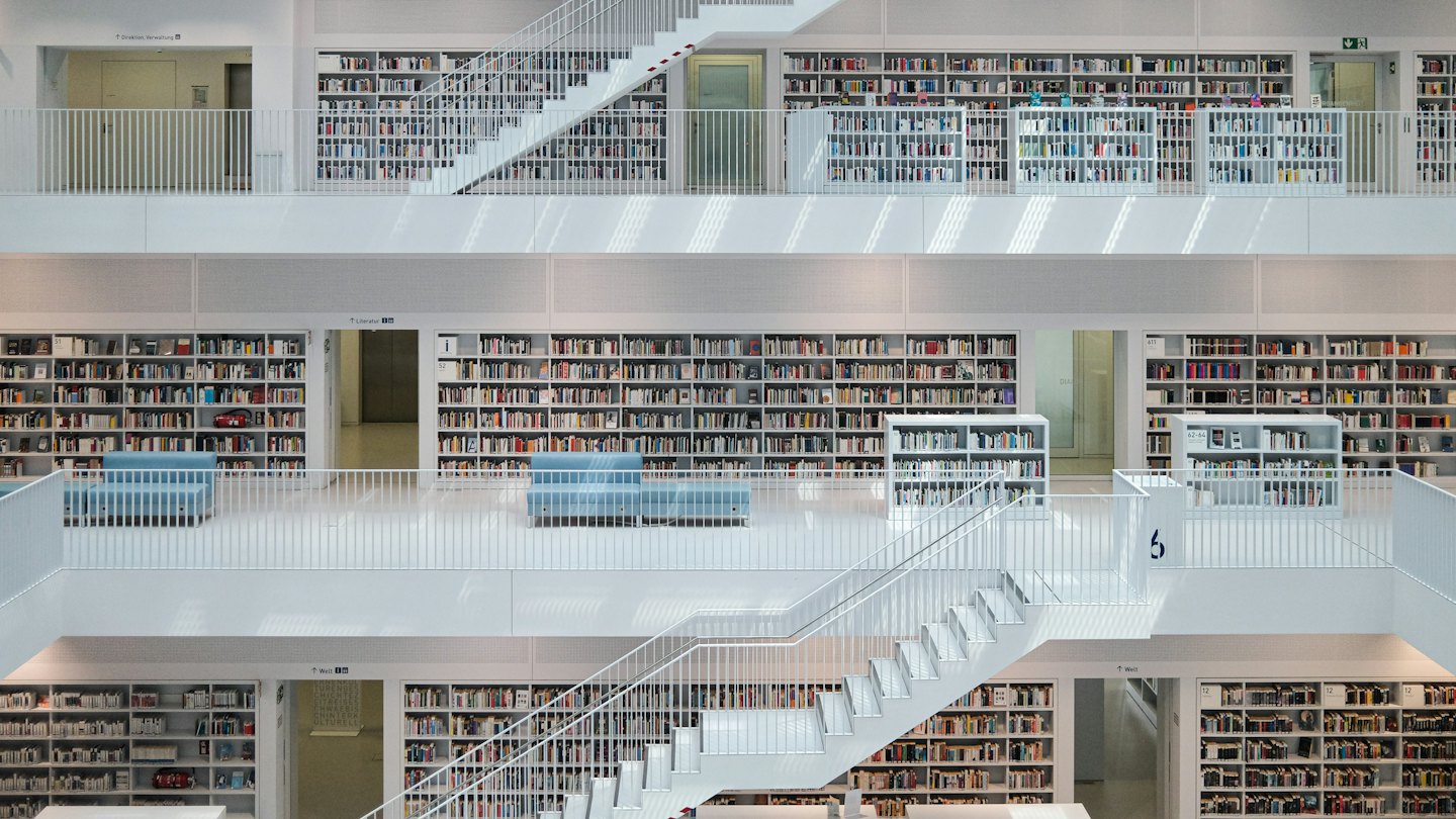 Nowoczesne wnętrze biblioteki z białymi regałami i niebieskimi miejscami do siedzenia.